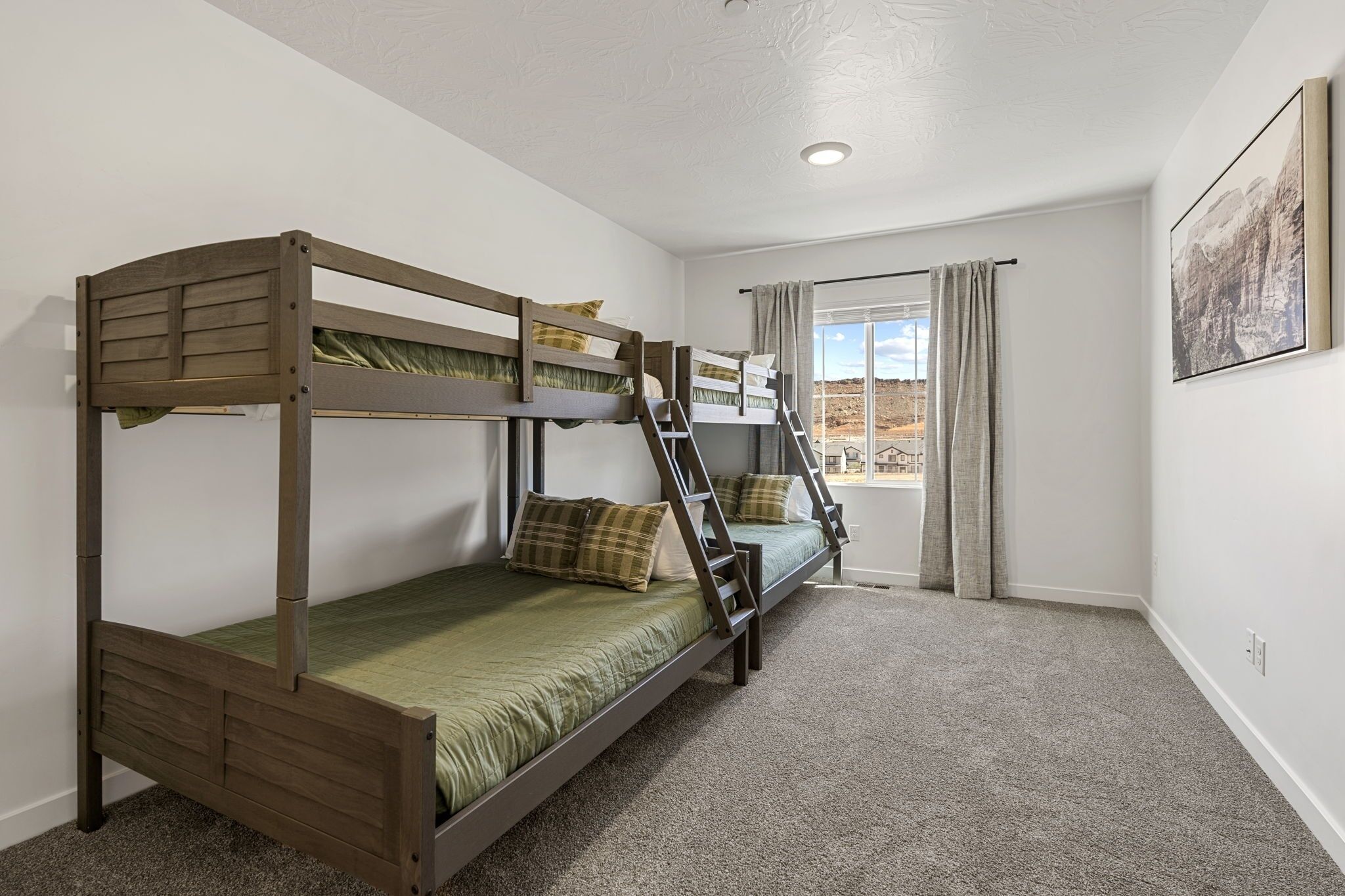 A bunk bed room with a window and curtains, carpeted floor, and a framed picture on the wall.