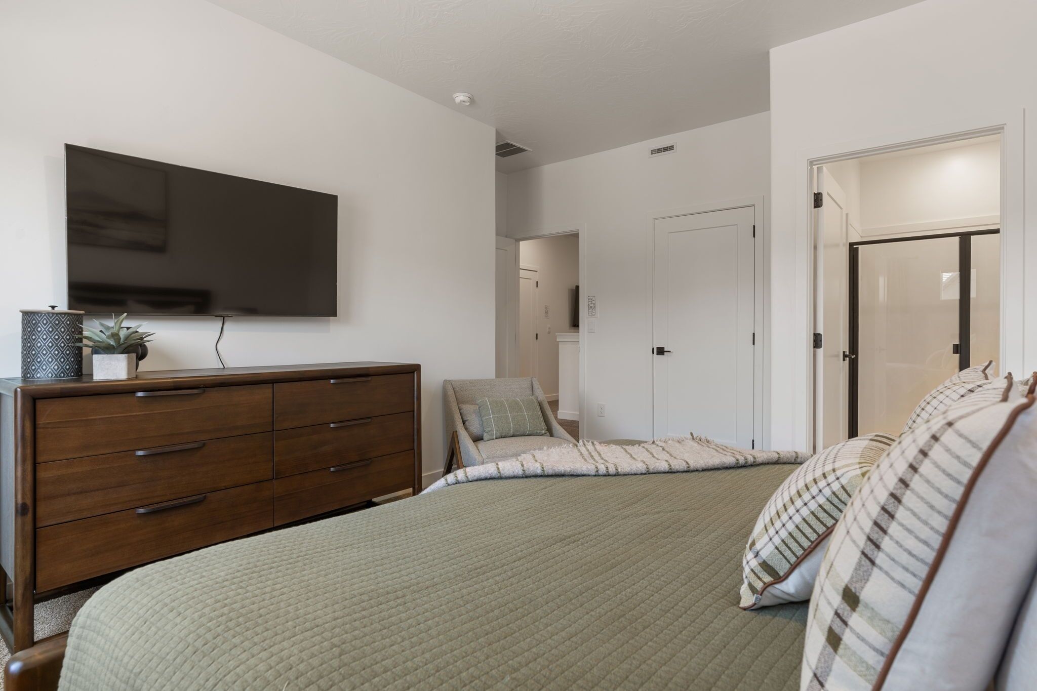 A bedroom with a bed, a dresser, a chair, a television, and a door.