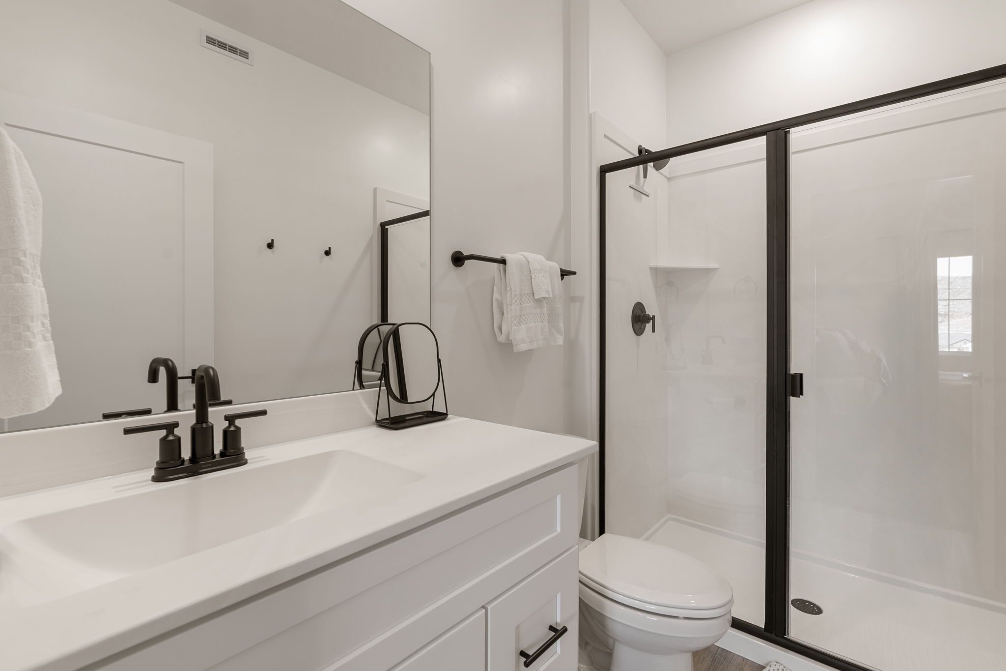 A modern bathroom with a white vanity, a black faucet, a glass shower enclosure, and a white toilet.
