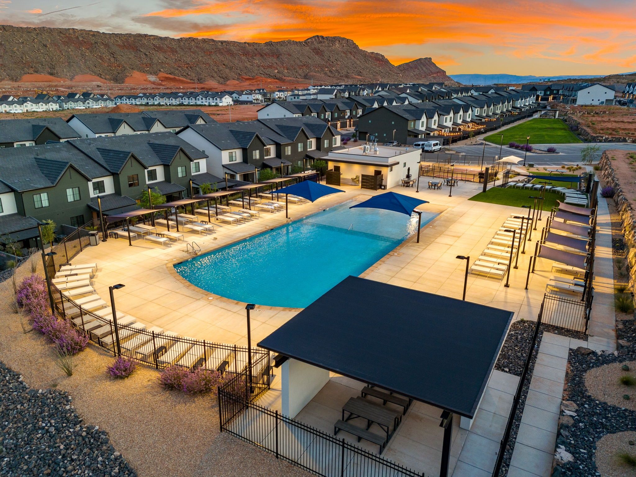 A residential area with a swimming pool, houses, and a hilly landscape in the background.