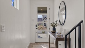 A hallway with a white door, a mirror, a small table with a vase of flowers, and a wooden staircase. - Sunseekers Escape 4 Bedroom Townhouse (Washington)