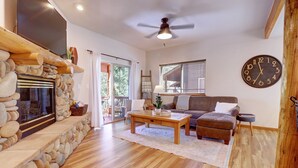 A living room with a stone fireplace, wooden coffee table, and a large clock on the wall.