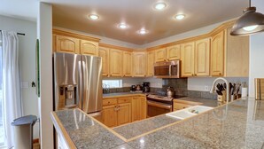 A modern kitchen with granite countertops, stainless steel appliances, wooden cabinets, and a large island with a sink.