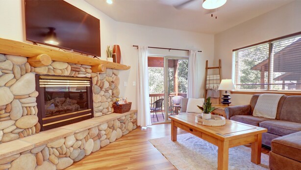 A cozy living room with a stone fireplace, wooden flooring, a comfortable sofa, and a television mounted above the fireplace.