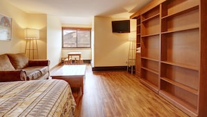 Une chambre à coucher avec un lit, une armoire en bois, une télévision et une fenêtre donnant sur les montagnes.