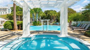Un área de piscina con un pérgola, palmeras y sillas de descanso.
