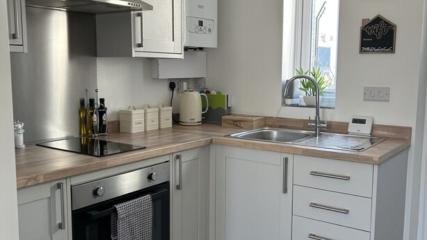 Een moderne keuken met witte kastjes, een roestvrijstalen afzuigkap, een inbouwoven, een spoelbak en een klok aan de muur.