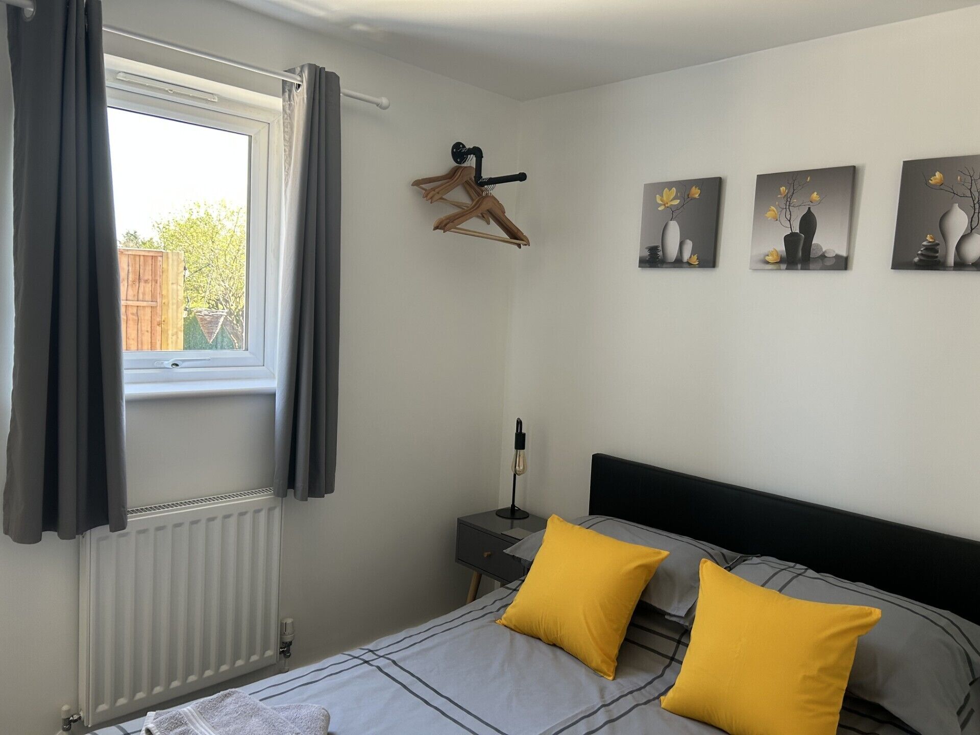 Une chambre à coucher comprenant un lit, un radiateur, une fenêtre avec des rideaux, une table de chevet et des œuvres d’art murales.