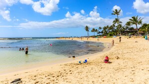 A beach with clear blue water, sandy shore, and palm trees. - Kauai Kiahuna Plantation #418 1 Bedroom Condo (Koloa)