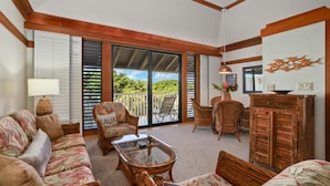 A spacious living area with a sofa, chairs, a coffee table, and a cabinet. There is a sliding glass door leading to a balcony with a view of greenery. - Kauai Kiahuna Plantation #418 1 Bedroom Condo (Koloa)