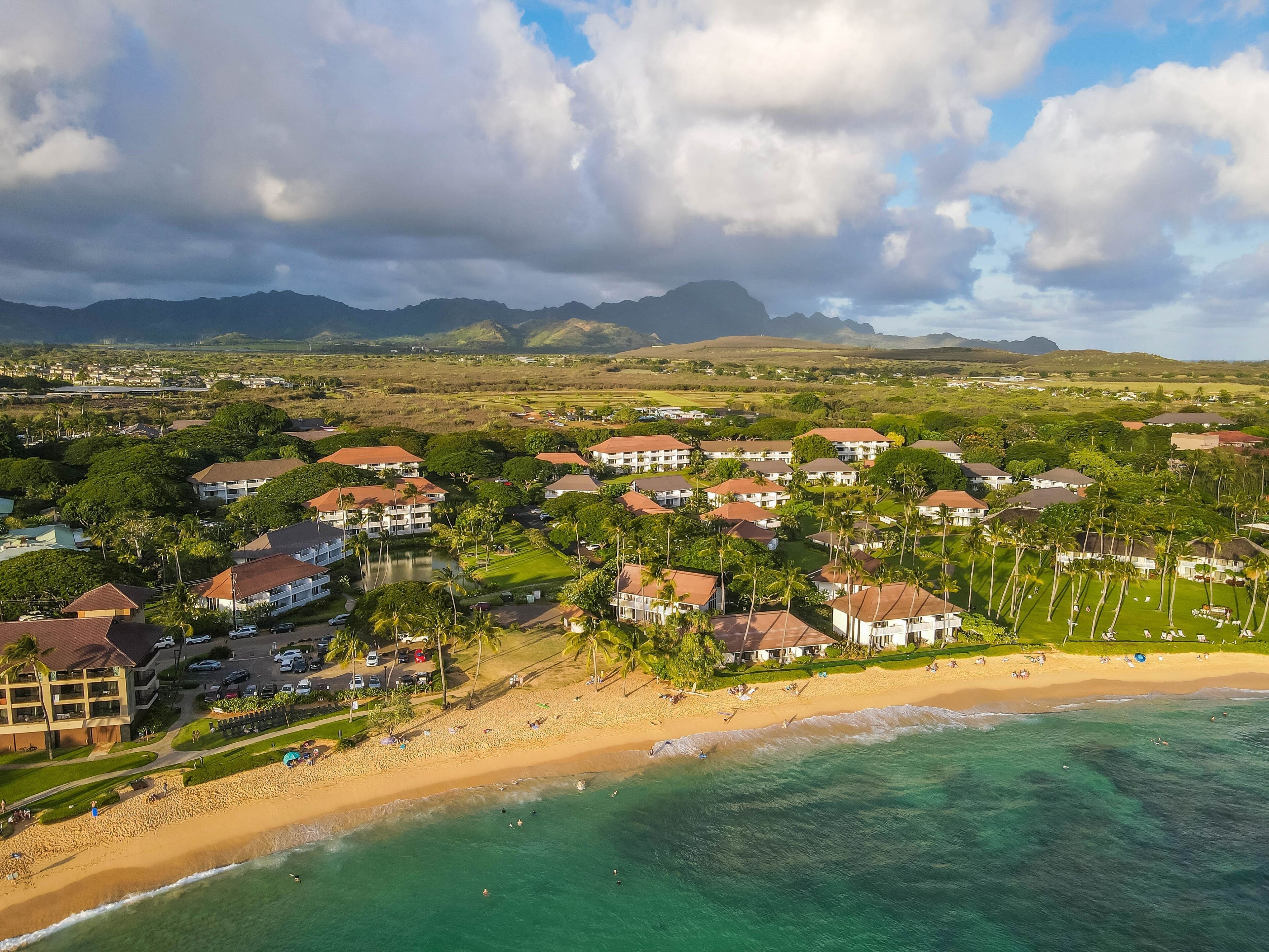 A coastal resort with beachfront villas, a sandy beach, and a view of distant mountains.