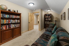 Un salón acogedor con una amplia estantería, un sofá estampado y una puerta de madera que da a otra habitación.