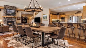 A spacious dining area with a wooden table and chairs, a fireplace, and a stone wall. - Alpine 5 Br Retreat / Hot Tub & Mountain Vistas (Big Sky)