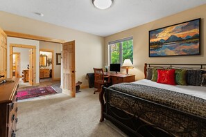 A bedroom with a bed, desk, chair, and a painting on the wall.