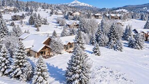 A snow-covered mountain town with wooden houses and a prominent mountain peak in the background. - Alpine 5 Br Retreat / Hot Tub & Mountain Vistas (Big Sky)