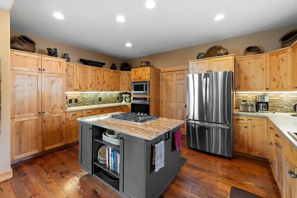 A modern kitchen with wooden cabinets, a central island with a stove, stainless steel appliances, and a stone backsplash.