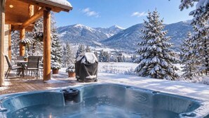 A wooden cabin with a hot tub and outdoor seating area, surrounded by snow-covered trees and mountains. - Alpine 5 Br Retreat / Hot Tub & Mountain Vistas (Big Sky)