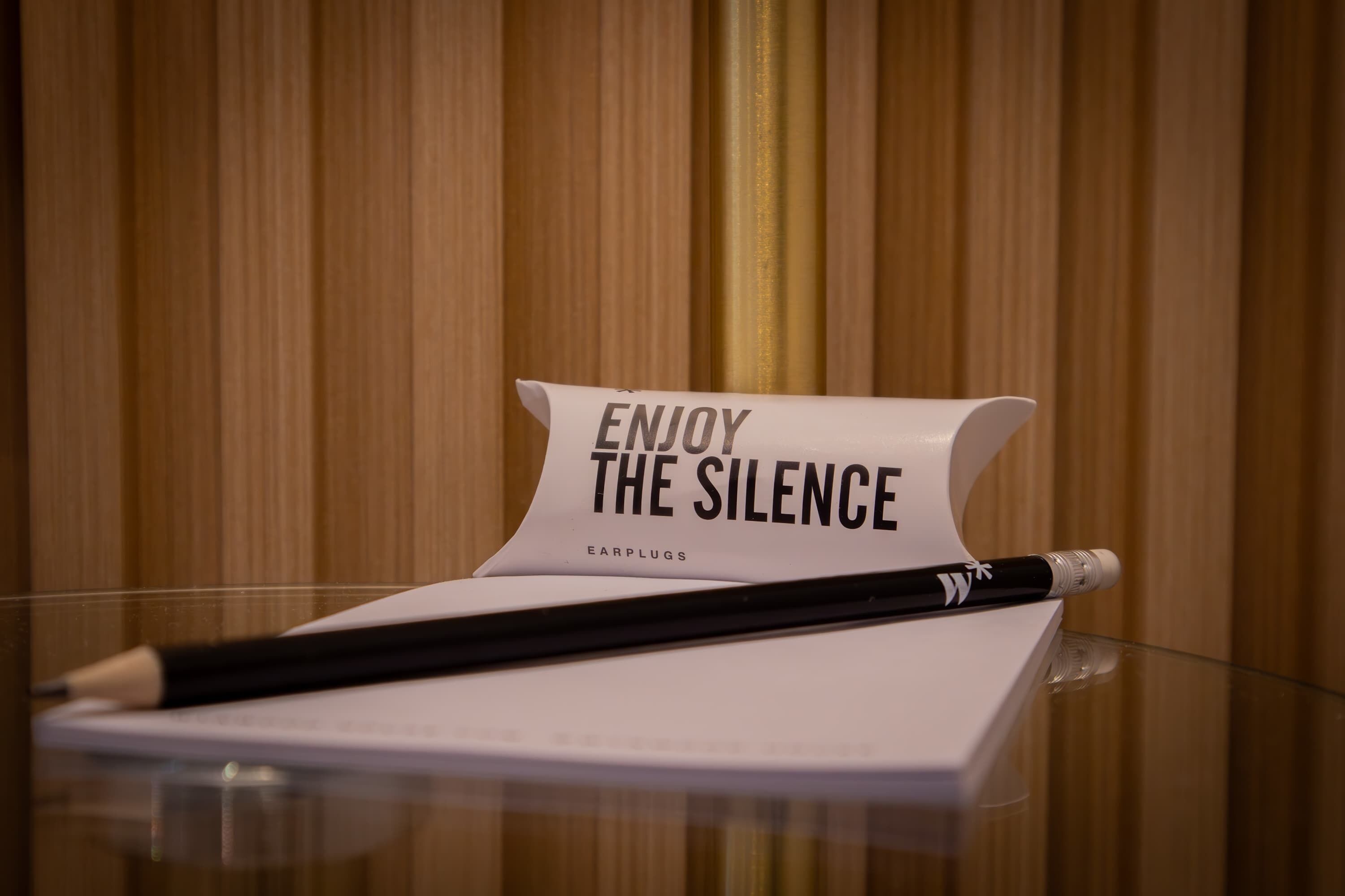 A piece of paper with the text 'ENJOY THE SILENCE' and a pencil on a glass surface.