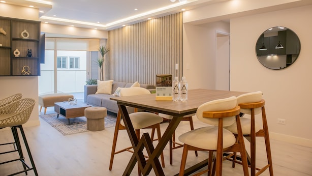 A modern living room with a wooden dining table, cushioned chairs, a sofa, and a large mirror on the wall. - w Bright 3BR w Balcony in Vibrant Miraflores (Lima)