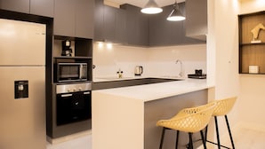 A modern kitchen with dark cabinets, a white countertop, a built-in oven, a microwave, and two bar stools. - w Bright 3BR w Balcony in Vibrant Miraflores (Lima)