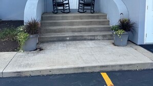 A building entrance with a white door, two rocking chairs, and potted plants on the steps.