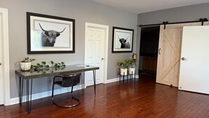 A modern interior with a wooden floor, a glass-top table with chairs, framed artwork, and a sliding barn-style door.