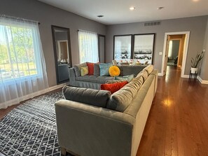 A spacious living room with a large grey sofa, a patterned rug, and a view of a scenic landscape through the windows. - Spacious 2 Bedroom Upstairs Apt in Lexington / Mansfield Monthly Rates Available (Mansfield)