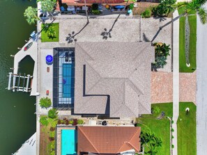 An aerial view of a property with a swimming pool, a dock, and a landscaped area with palm trees.