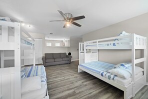A room with bunk beds, a ceiling fan, a gray sofa, and a wooden floor.