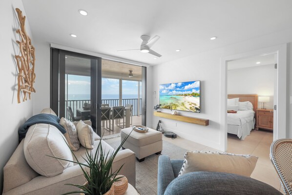 A modern living room with a sofa, ottoman, and a flat-screen TV mounted on the wall.