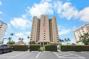 A tall hotel with a central flagpole, parking lot, and palm trees.