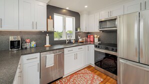 A modern kitchen with white cabinets, stainless steel appliances, and a large window.
