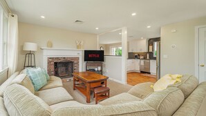 A living room with a fireplace, a television, and a kitchen in the background.