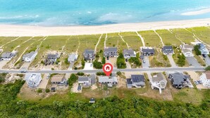An aerial view of a coastal residential area with houses, a road, and a beach.