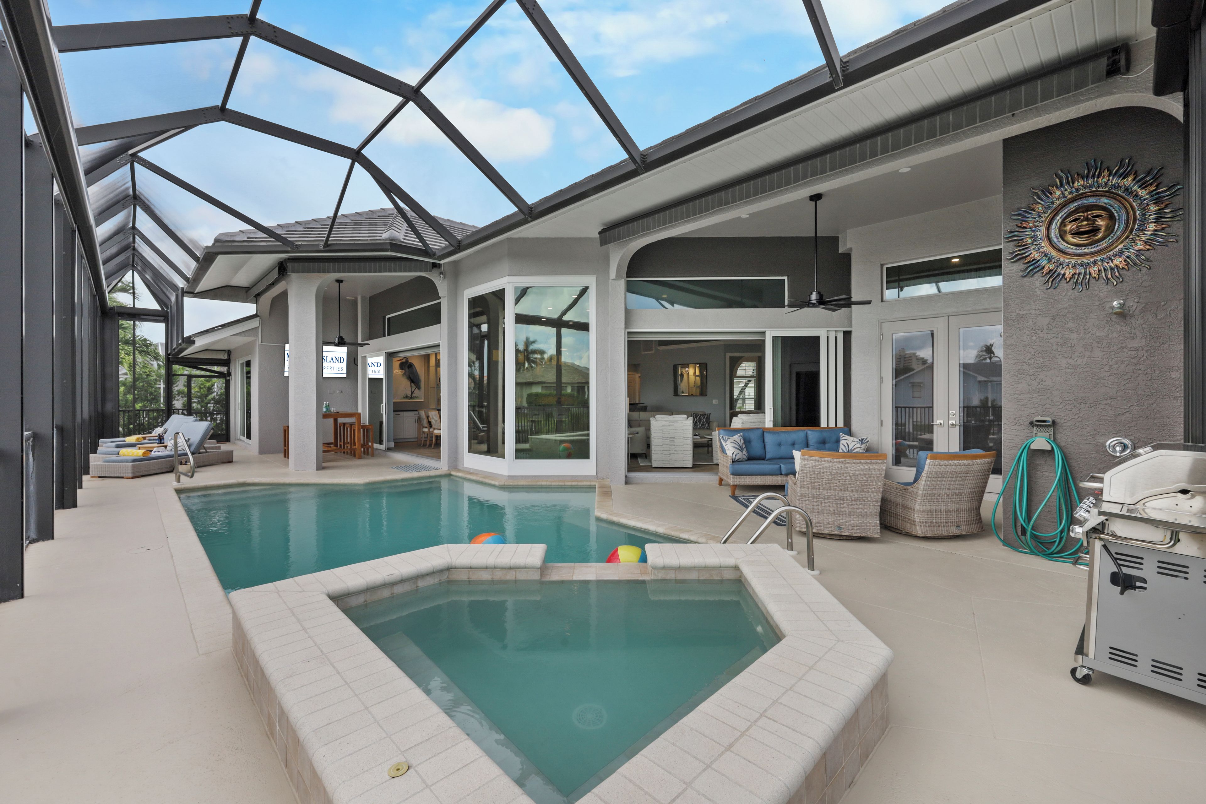 A modern indoor pool area with a glass ceiling, lounge chairs, and a barbecue grill.