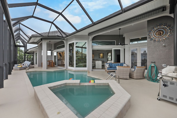A modern indoor pool area with a glass ceiling, lounge chairs, and a barbecue grill.