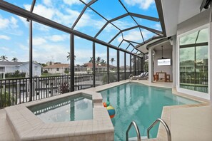 An indoor swimming pool with clear views of the surrounding neighborhood, including houses and palm trees. - Walk to beach waterfront home w/ pool, spa & kayaks (Marco Island)