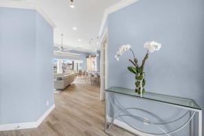 A modern interior with a glass console table, white orchids, and a dining area in the background.