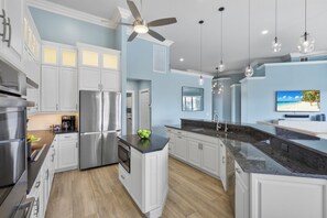 A modern kitchen with white cabinetry, stainless steel appliances, a central island, and pendant lighting. - Walk to beach waterfront home w/ pool, spa & kayaks (Marco Island)