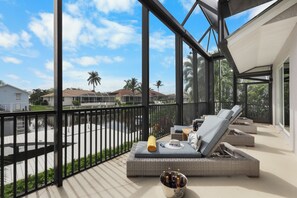 Un balcon avec des fauteuils de jardin en osier, un seau rempli de bouteilles et un chapeau posé sur un coussin.