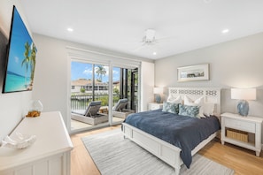 A bedroom with a bed, nightstands, a ceiling fan, a large window, and a view of the outdoors.