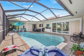 A pool area with lounge chairs, a table, and a grill. - Direct Boating Modern Home | Heated Pool & Kayaks (Marco Island)