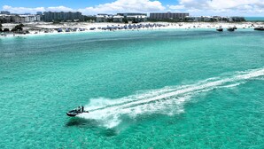 A beach with clear turquoise water, a jet ski, and a row of buildings in the background. - Charming Coastal Retreat Mag House 410 | Steps to the Beach + Pool Access! (Destin)