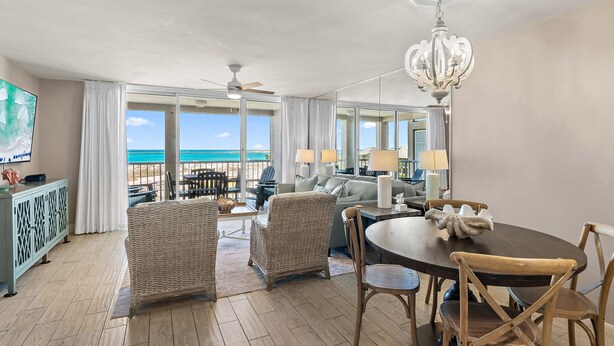 A spacious room with a dining table, chairs, a chandelier, and a view of the ocean. - Charming Coastal Retreat Mag House 410 | Steps to the Beach + Pool Access! (Destin)