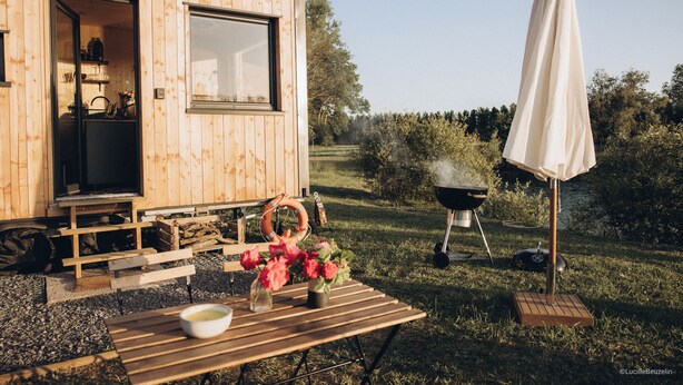 En træhytte med et stort vindue, grill og et picnicbord med blomster.