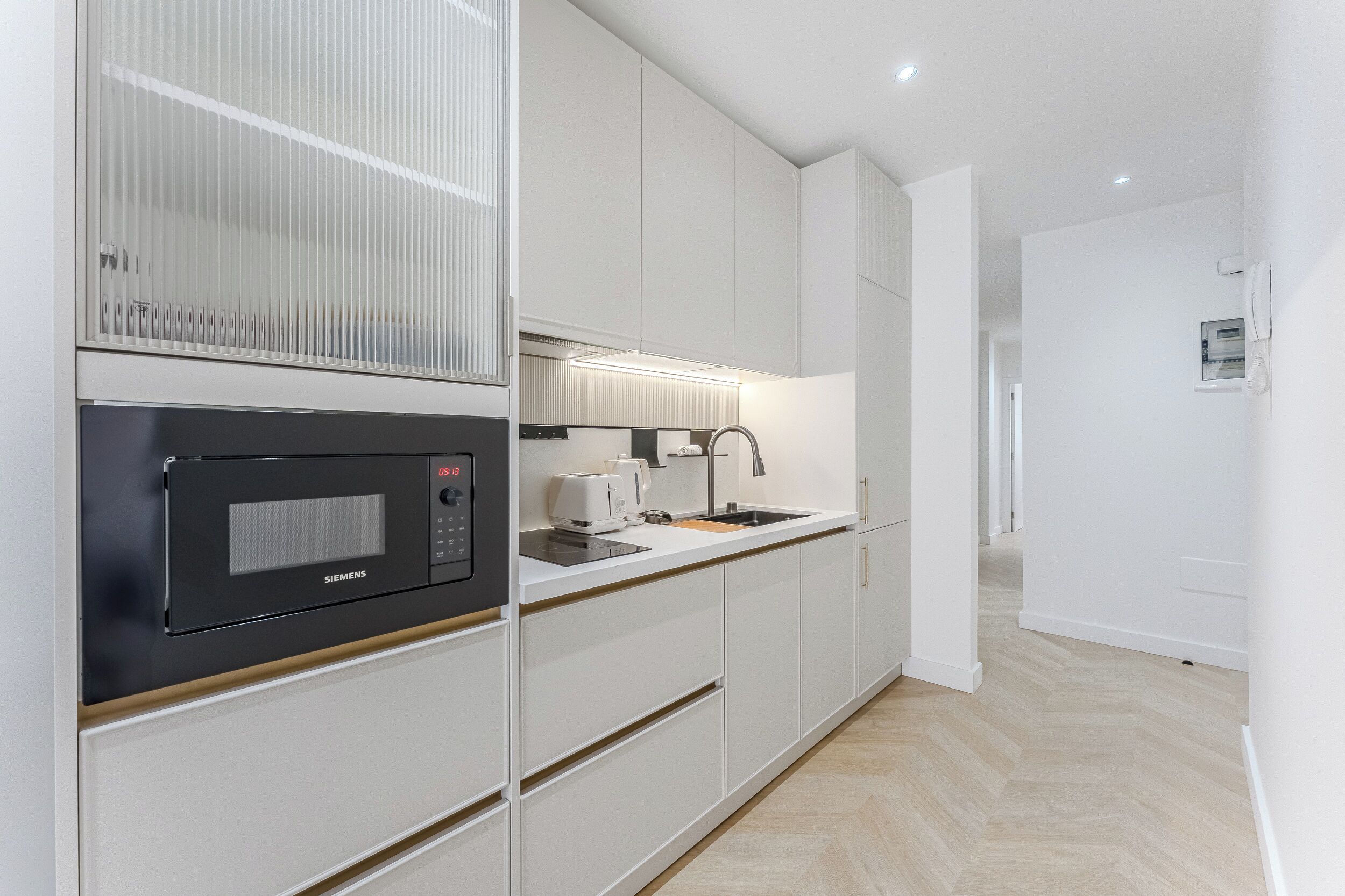 Una cocina moderna con armarios blancos, un microondas integrado y un lavamanos.
