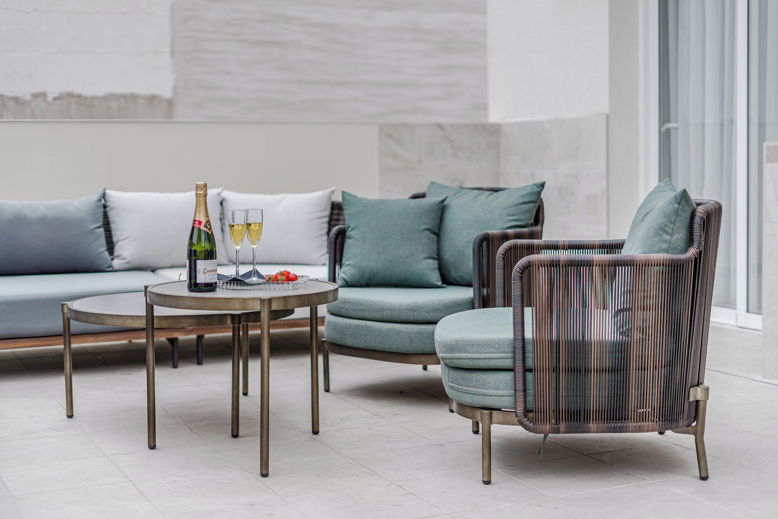 A modern living room with a sofa, armchair, and round table with a bottle and glasses.