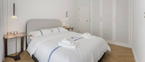 Et pænt hotelværelse med en stor seng, et natbord, et garderobeskab og en hængende lysarmatur.