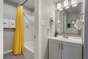 Une salle de bain avec un rideau de douche jaune, un lavabo blanc, un miroir et un sèche-cheveux.