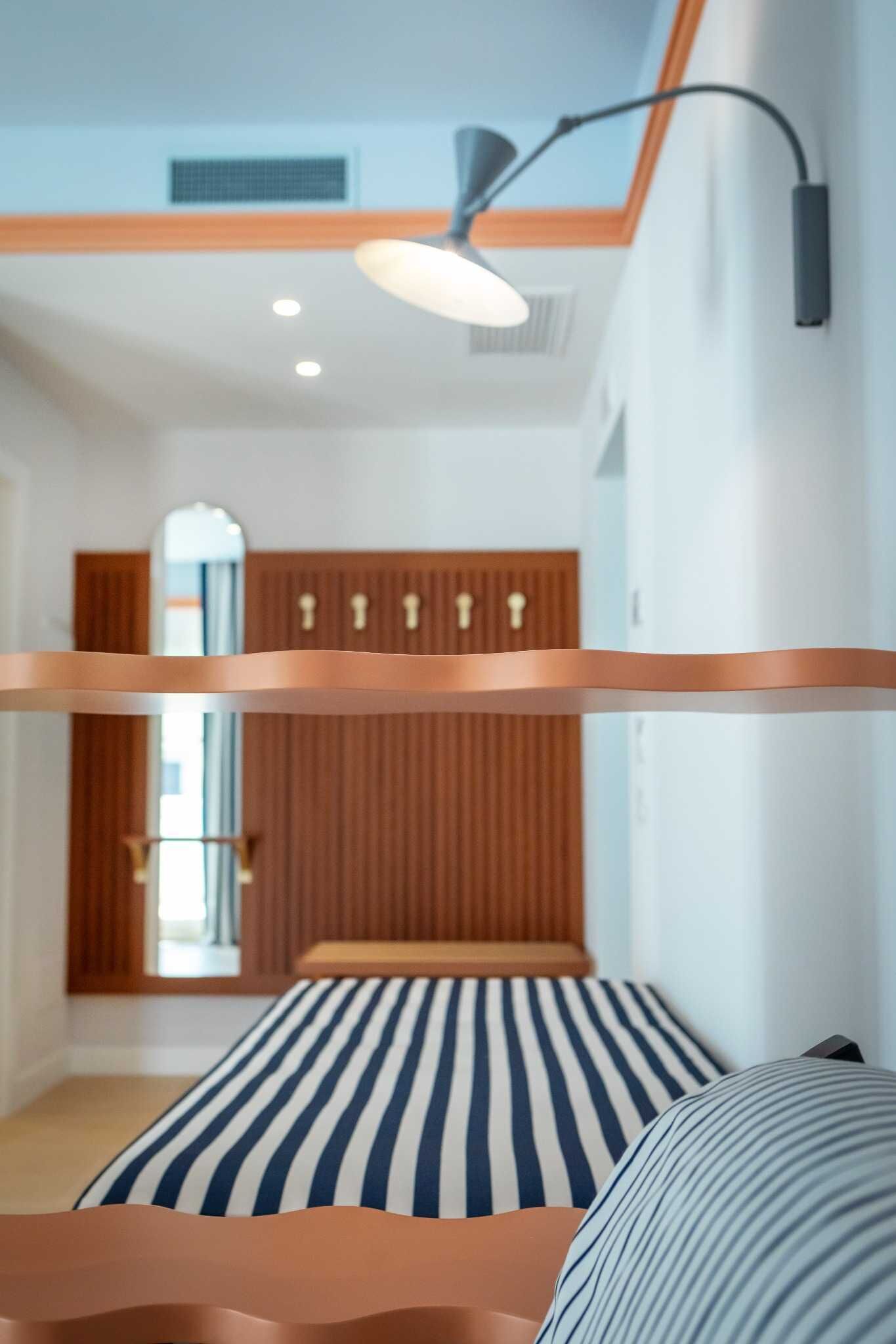 Un lit superposé avec un matelas à rayures, une lampe suspendue au plafond et un mur recouvert de panneaux en bois.